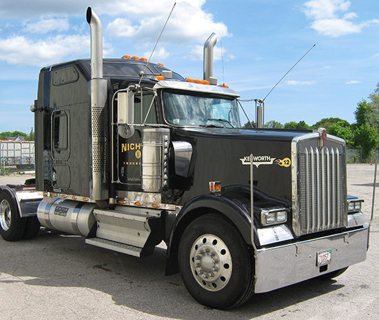 Black Nichols Kenworth tractor with gold lettering under a blue New England sky